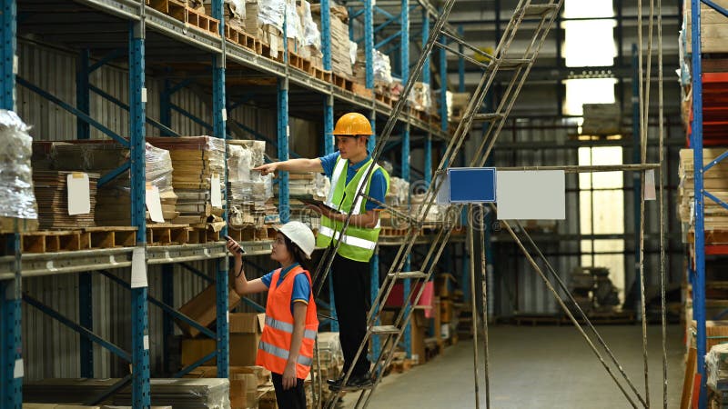 Male and female workers wearing hardhats and reflective jackets checking inventory boxes on shelf with barcode scanner royalty free stock image