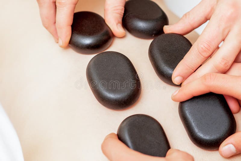 Male four hands laying large new oval black hot stones for back massage on female back in spa salon. Male four hands laying large new oval black hot stones for back massage on female back in spa salon