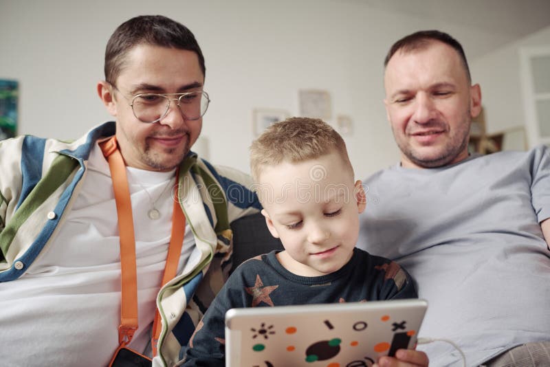 Male gay couple and adopted boy with tablet at home