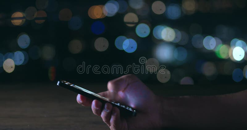 Male hand scrolling browsing social networks on phone on background of lights of night city. Cinematic shot male scroll