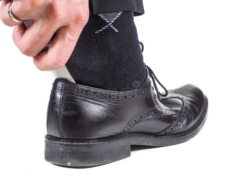 Male hand entering black sock on foot into leather shoe with shoehorn