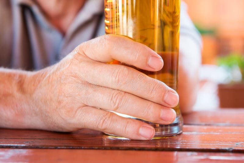 Male hand holding glass of freshly tapped beer, close up