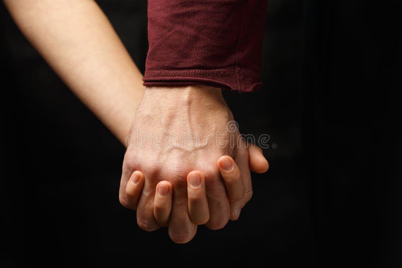 male hand holds female hand on dark background