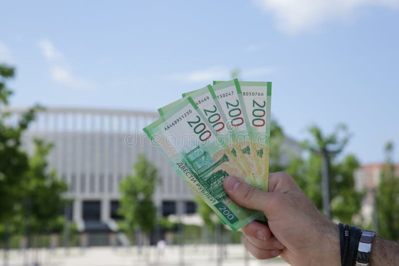 Male hand holds a new Russian banknote two hundred rubles on the background of a building and blue sky. Cash paper money stock image Male hand holds a new Russian banknote two hundred rubles on the background of a building and blue sky. Cash paper money stock image