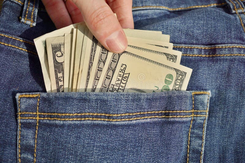 Male hand inserting or withdrawing heap of American money US currency, USD in the back pocket of blue jeans with yellow stitchin