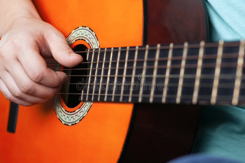 Male hand plays acoustic guitar strings. learning to play a musical instrument orange color close-up royalty free stock image