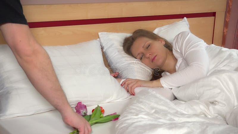 Male hand put bouquet of tulip flowers near sleeping female woman on bed