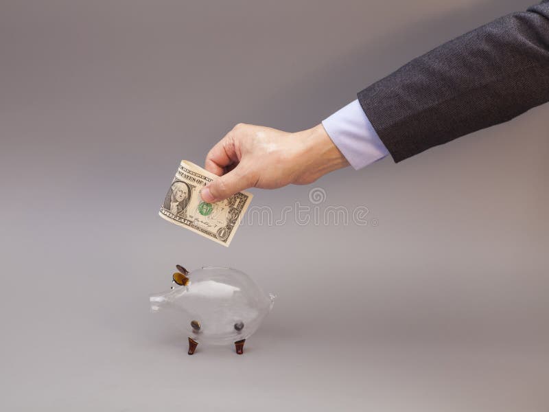 Male hand putting one dollar bill into glass piggy bank isolated on gray