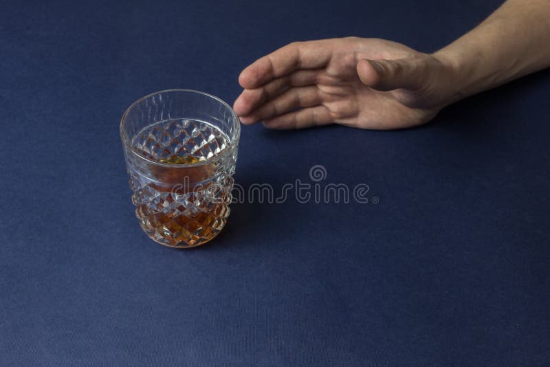 Male hand reaching for a glass with alcohol, close-up, blue background stock photography
