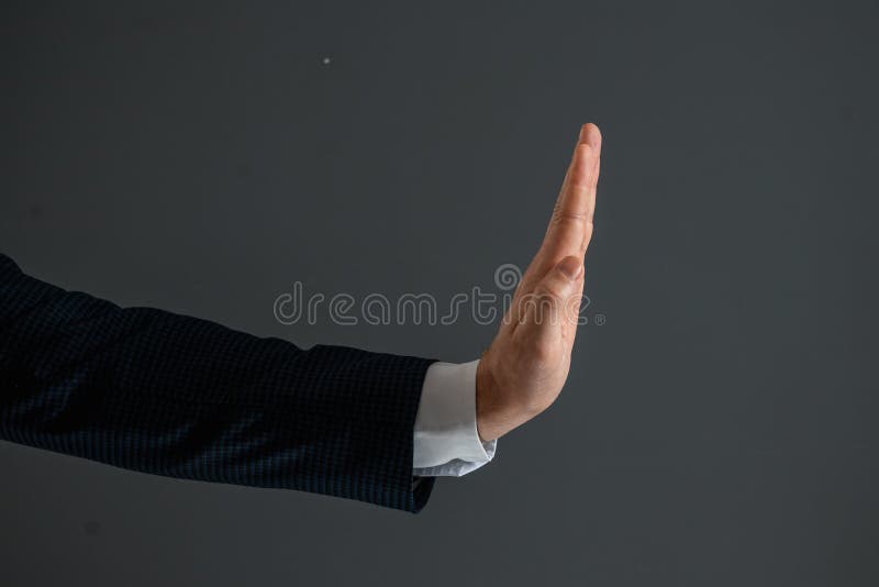 Male hand in a suit shows the palm of the stop gesture on a gray background. Stop concept, close-up