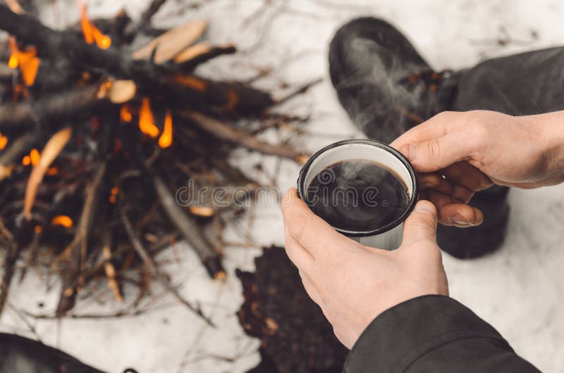 Male hands hold a mug of coffee near a burning campfire. Concept hike, walk, trip in winter royalty free stock photography Male hands hold a mug of coffee near a burning campfire. Concept hike, walk, trip in winter royalty free stock photography