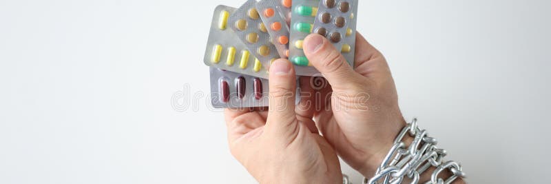 Male hands tied with chain and hold various medical pills closeup. Male hands tied with chain and hold various medical pills. Drug addiction concept