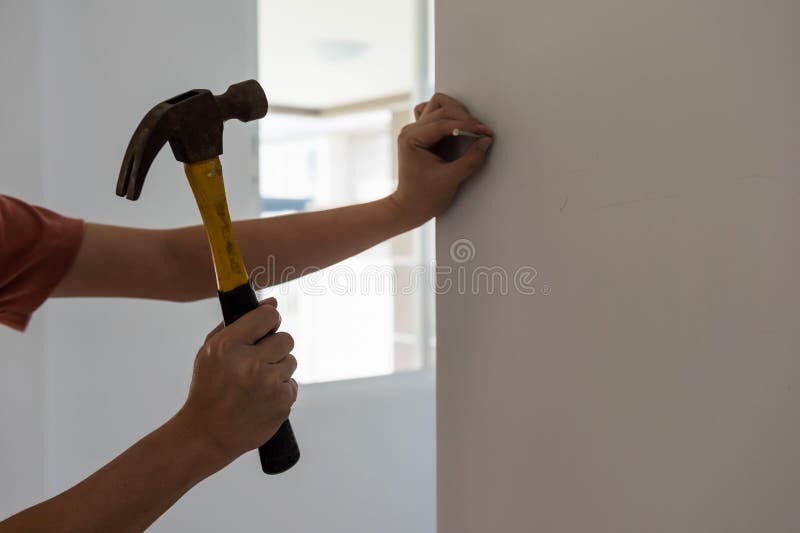 Male house owner hammering a nail into blank white wall. Concept of new home decoration stock images Male house owner hammering a nail into blank white wall. Concept of new home decoration stock images