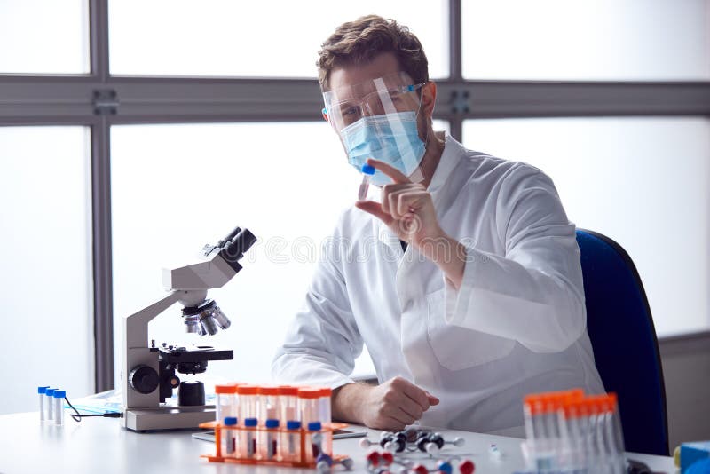 Male Lab Worker Wearing PPE Analysing Blood Samples in Laboratory with