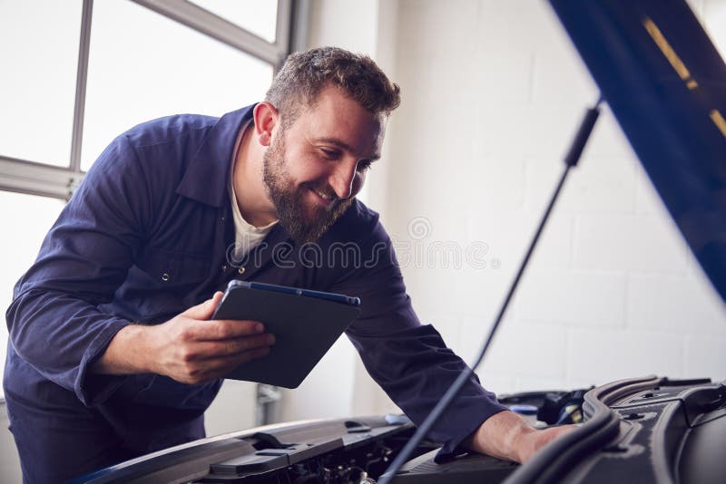 Male Mechanic in Garage Using Diagnostic Software on Digital Tablet To