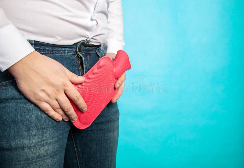 A male office worker in a white shirt holds a red heating pad with hot water near his groin against a blue background. The concept of urolithiasis, inflammation of the bladder in men. Copy space for text, varicocele