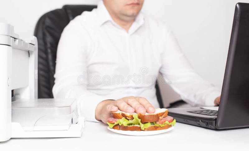 Male office worker in a white shirt with a sandwich in his hand. Workplace snack, breakfast stock images