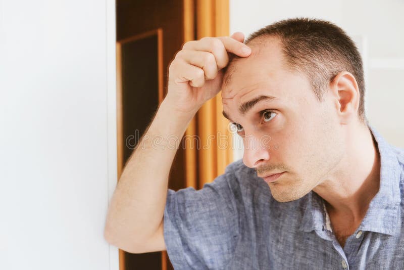 Young man looking at mirror worry about balding.