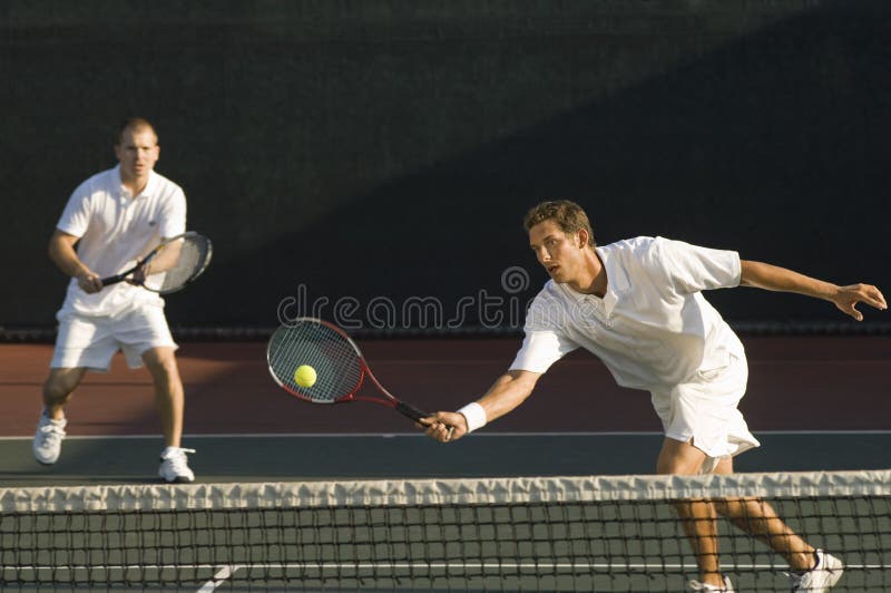 Mixed doubles player hitting tennis ball with partner in the background. Mixed doubles player hitting tennis ball with partner in the background