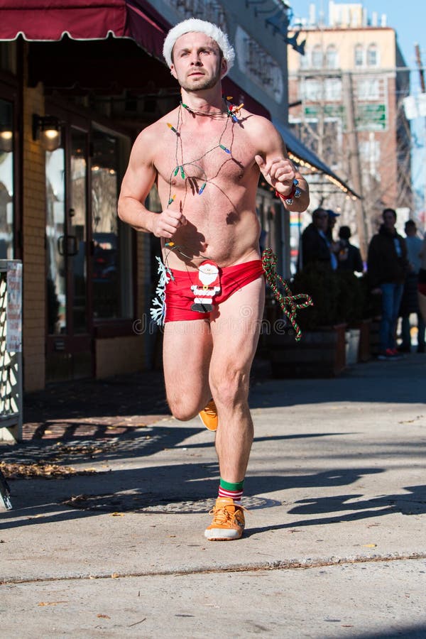 Atlanta, GA, USA - December 10, 2016: A male runner wearing Christmas lights, a Santa hat and a skimpy swimsuit jogs down a city street at the Santa Speedo Run, an annual charity fundraiser, on December 10, 2016 in Atlanta, GA. Atlanta, GA, USA - December 10, 2016: A male runner wearing Christmas lights, a Santa hat and a skimpy swimsuit jogs down a city street at the Santa Speedo Run, an annual charity fundraiser, on December 10, 2016 in Atlanta, GA.