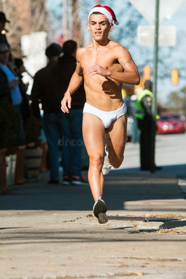 Atlanta, GA, USA - December 10, 2016: A male runner wearing a white speedo swimsuit jogs down a city street at the Santa Speedo Run, an annual charity fundraiser, on December 10, 2016 in Atlanta, GA. Atlanta, GA, USA - December 10, 2016: A male runner wearing a white speedo swimsuit jogs down a city street at the Santa Speedo Run, an annual charity fundraiser, on December 10, 2016 in Atlanta, GA.