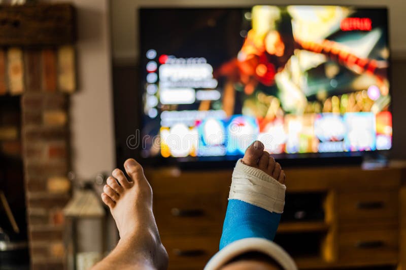 Male sat on sofa watching tv with a cast on foot from fifth metatarsal surgery..