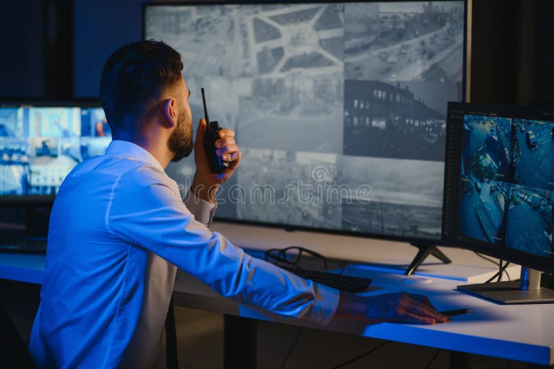 Male Security Guard Talking On Walkie talkie While Monitoring Multiple CCTV Footage On Computer stock photos