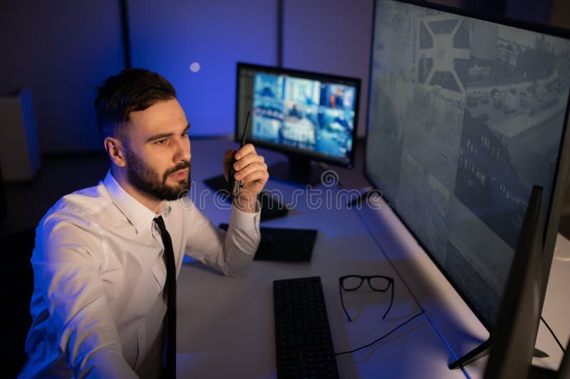 Male Security Guard Talking On Walkie talkie While Monitoring Multiple CCTV Footage On Computer stock images