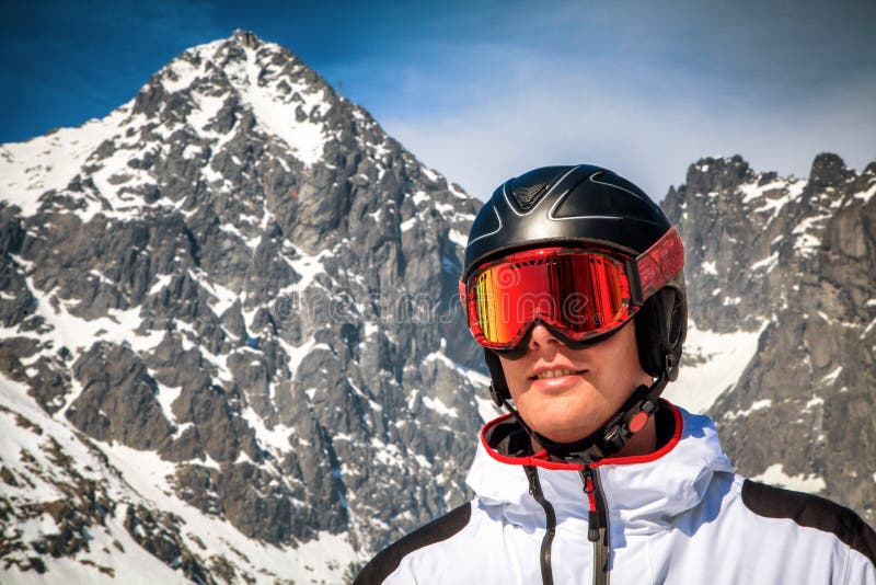 Muž lyžiar s lyžiarskymi okuliarmi helmou zasnežený vrchol na pozadí