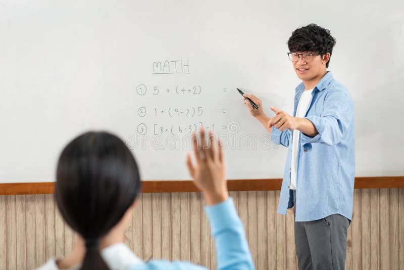 Male tutor standing in front of whiteboard is smiling and pointing to him for ask question and asian young boy royalty free stock image