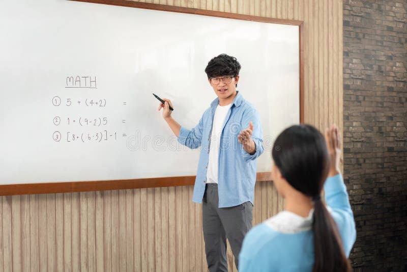 Male tutor standing in front of whiteboard is smiling and pointing to him for ask question and asian young boy stock photo