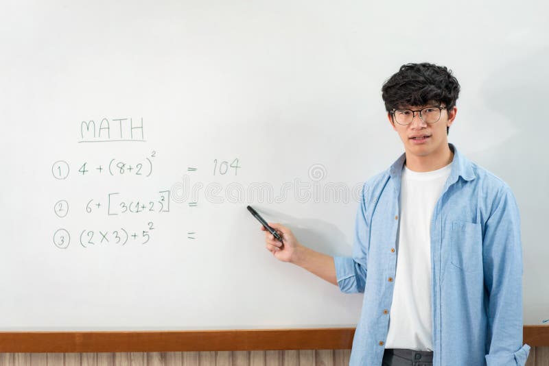 Male tutor standing in front of whiteboard and writing math equations on board to explaining new lesson stock photos