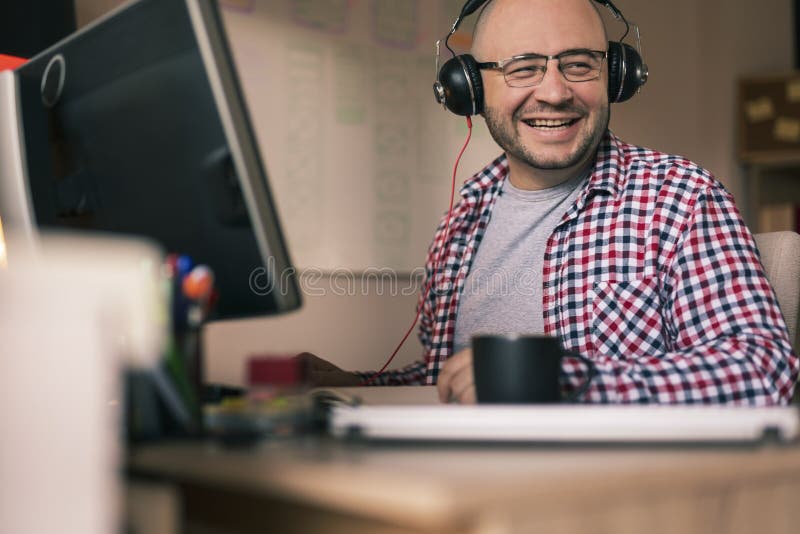 Male web designer working in an office. Male web designer sitting at his desk in an office, wearing headset and working; freelancer working from home stock photo