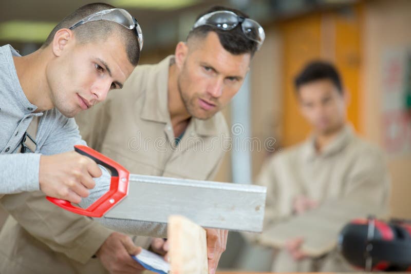 Male Woodworking Apprentice Cutting Wood with Manual Saw Stock Photo