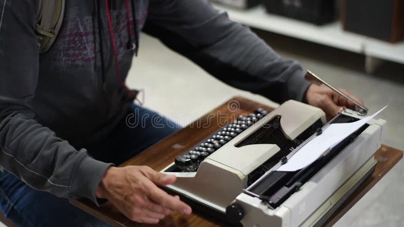 A male writer is typing on the keys of an old typewriter.