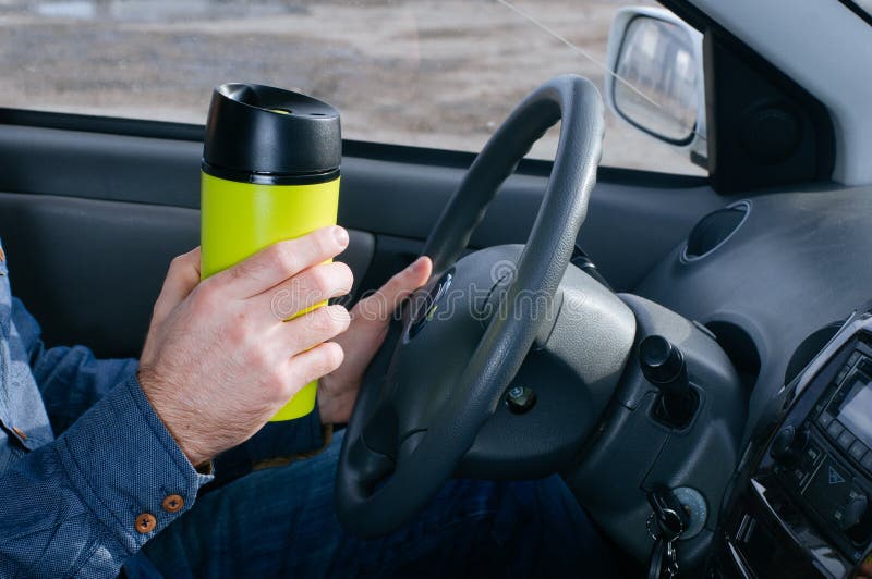 Close up of male`s hand holding thermo mug with hot coffee driving in a car. Close up of male`s hand holding thermo mug with hot coffee driving in a car