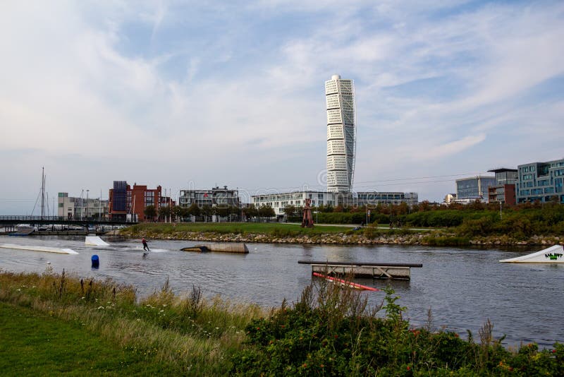 Malmö, Sweden - September 1, 2019: A person is practicing wake boarding in the canal close to the skyscraper Turning Torso, seen in the distance. Malmö, Sweden - September 1, 2019: A person is practicing wake boarding in the canal close to the skyscraper Turning Torso, seen in the distance.