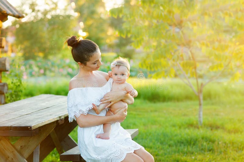 A mam? est? nutrindo sua crian?a na natureza Fam?lia feliz que senta-se no fundo do por do sol foto de stock A mam? est? nutrindo sua crian?a na natureza Fam?lia feliz que senta-se no fundo do por do sol foto de stock