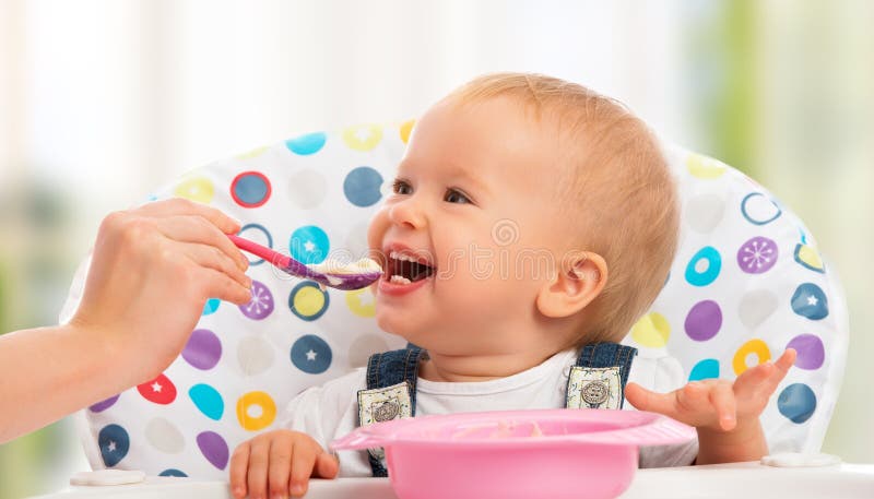 Mama fericită hrănește un copil amuzant din lingură stock images