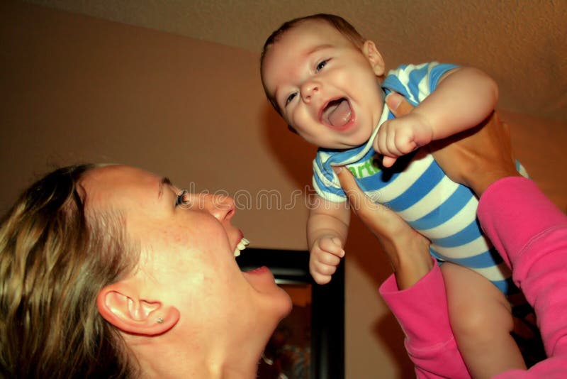 A moment of joy between a mother and son, a woman in a pink shirt holding up a baby boy dressed in a blue and white striped outfit, hoisting baby up in the air with big open smiles on both faces. A moment of joy between a mother and son, a woman in a pink shirt holding up a baby boy dressed in a blue and white striped outfit, hoisting baby up in the air with big open smiles on both faces