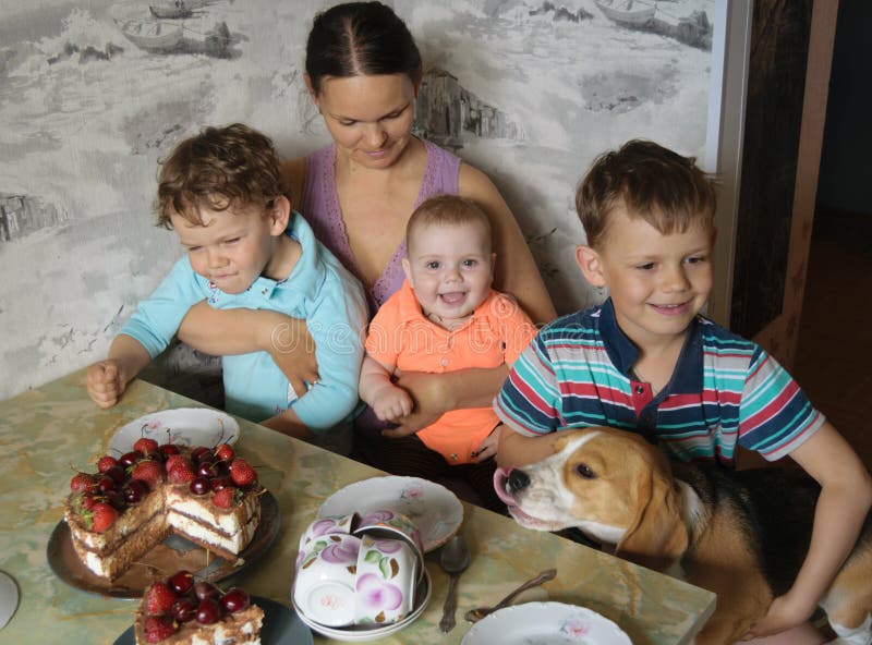 Mama z trzy dzieciakami i Beagle przy stołem w oczekiwaniu na jagodę zasychamy fotografia stock Mama z trzy dzieciakami i Beagle przy stołem w oczekiwaniu na jagodę zasychamy fotografia stock