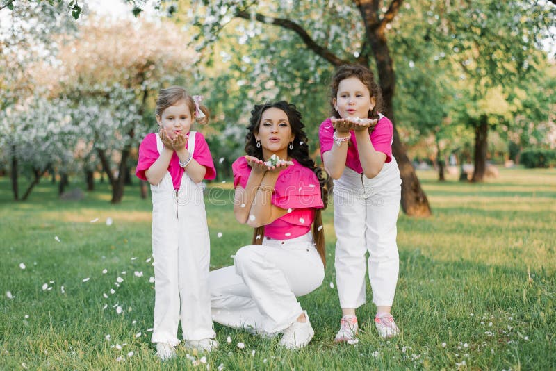 Maman mignonne et deux filles soufflant sur les pétales tombés des fleurs de pomme dans le jardin de printemps. activité extérieur images libres de droits