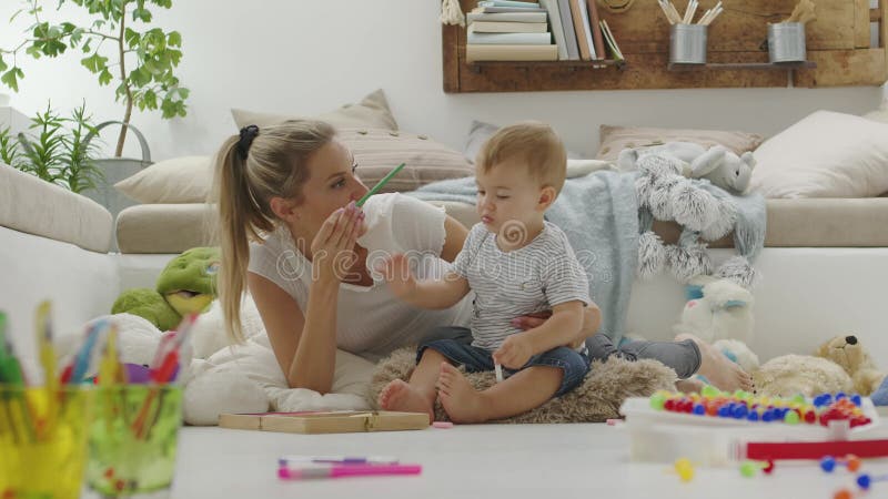 Maman souriante joyeuse joue avec son bébé avec des crayons et craies colorés jeu éducatif assis à la maison entre banque de vidéos