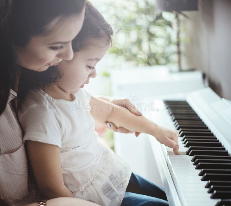 Mamma che insegna al suo gioco del piano della figlia immagine stock Mamma che insegna al suo gioco del piano della figlia immagine stock