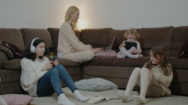 Mamma che lavora con computer portatili e bambini che usano dispositivi sul divano in camera d'appartamento. stock footage
