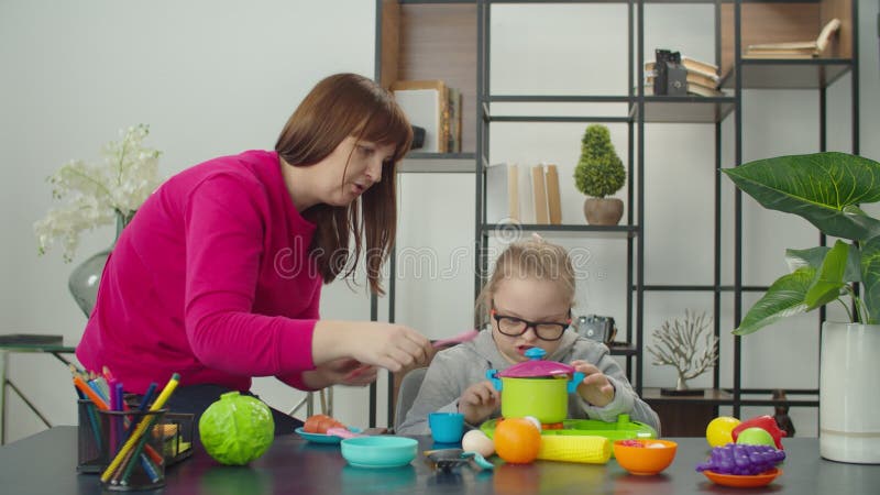 Mamma con figlia disabile che gioca a cucine con un set di giocattoli video d archivio