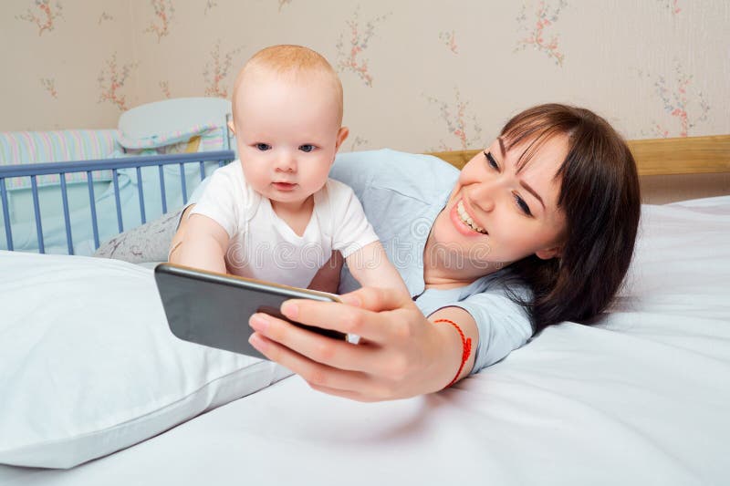 Mamma e bambino con il telefono sul letto nella stanza fotografie stock Mamma e bambino con il telefono sul letto nella stanza fotografie stock