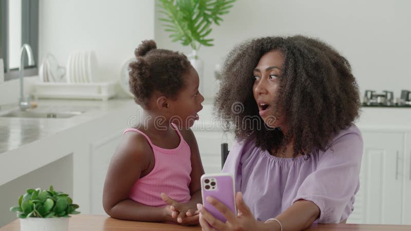 Mamma e figlia sedute vicine tra di loro guardando vignette su smartphone ed esprimendo emozioni a sorpresa da