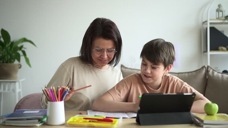 Mamma gör läxor och leker på bordet med en tablett i lägenheten spbd. stock video