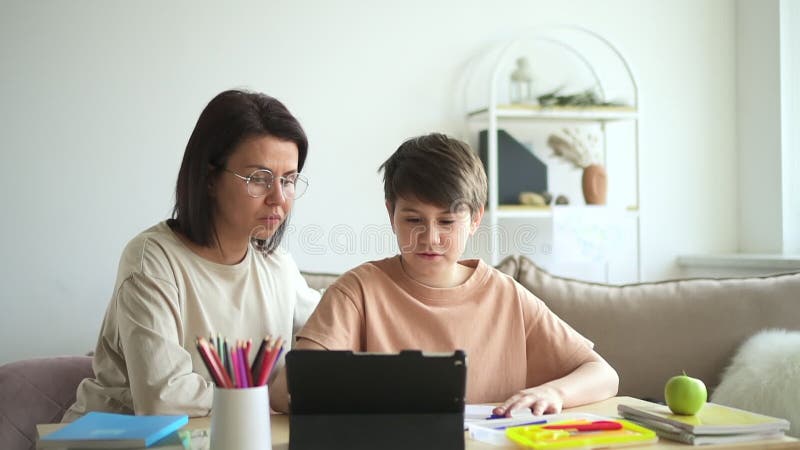 Mamma hjälper son med läxor med hjälp av en tablett för att studera spbd. överordnad bläddringsenhet online-sökning arkivfilmer